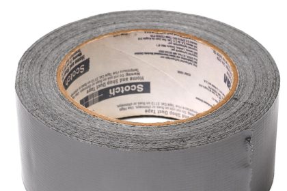 Egy tekercs szürke ragasztószalag, enyhén felemelt széllel, amelyen a Scotch márkajelzés látható a belső kartongyűrűn. A szalag textúrája látható, és a tekercs függőlegesen áll a fehér háttéren.
